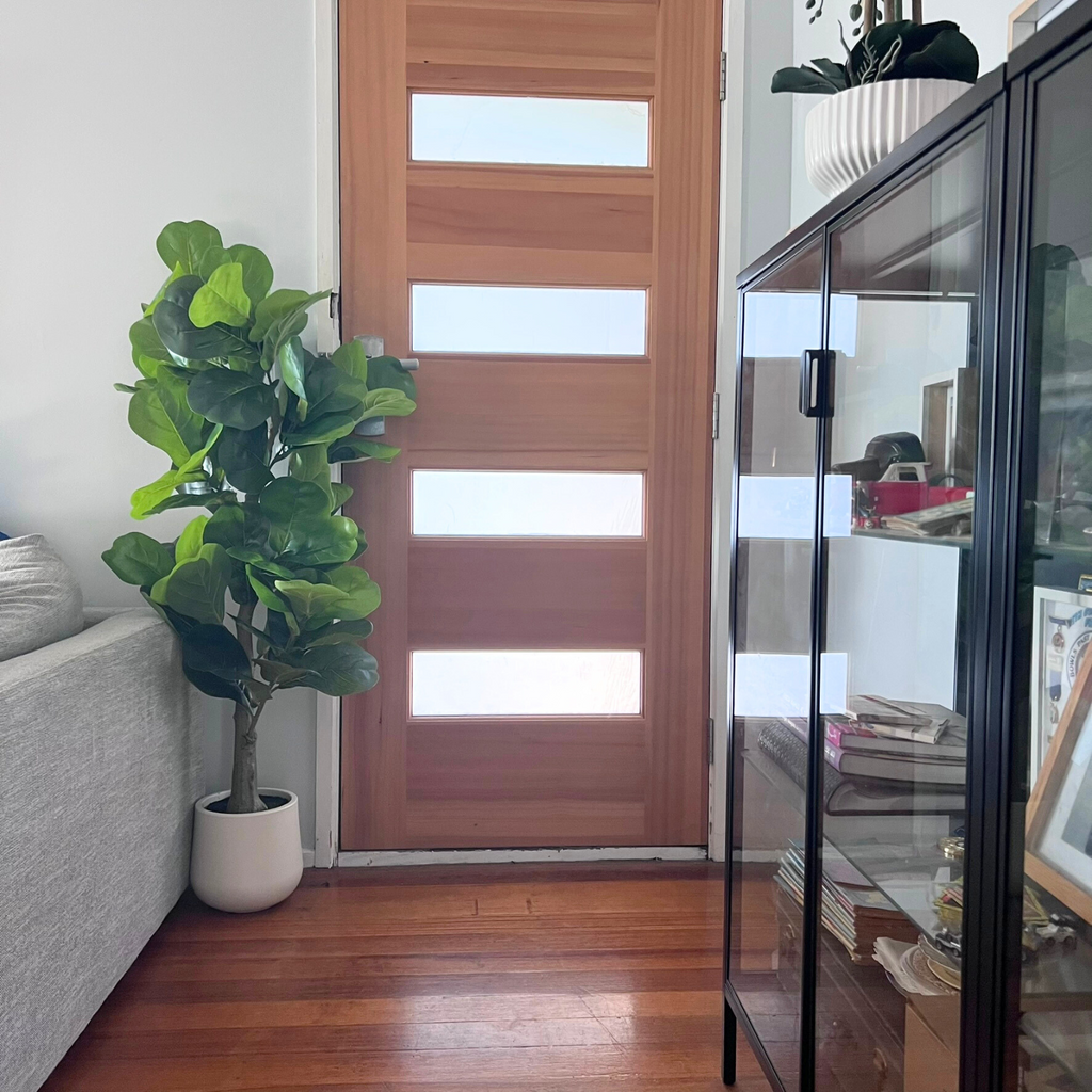 The artificial fiddle leaf fig tree styles in a living space next to a door 