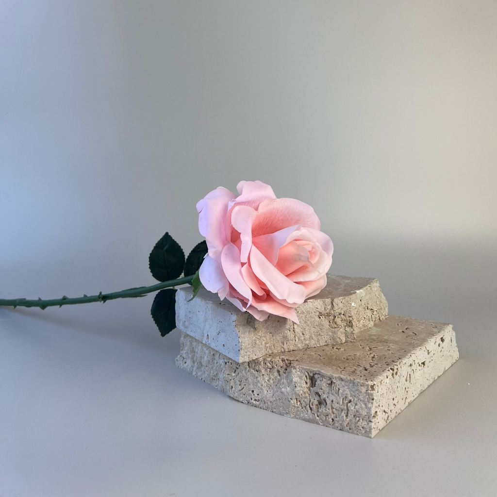Soft pink artificial  rose positioned on two light-coloured stones 