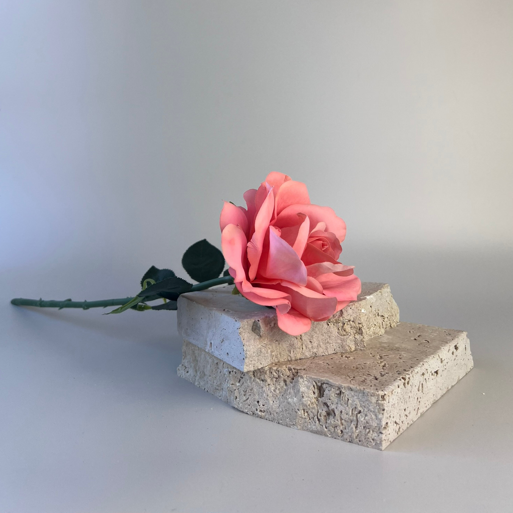 Artificial Flamingo coloured rose styled on top of two flat rocks 