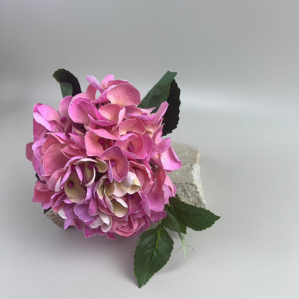 The artificial Hydrangea in the colour flamingo styled on a block with a beige background 