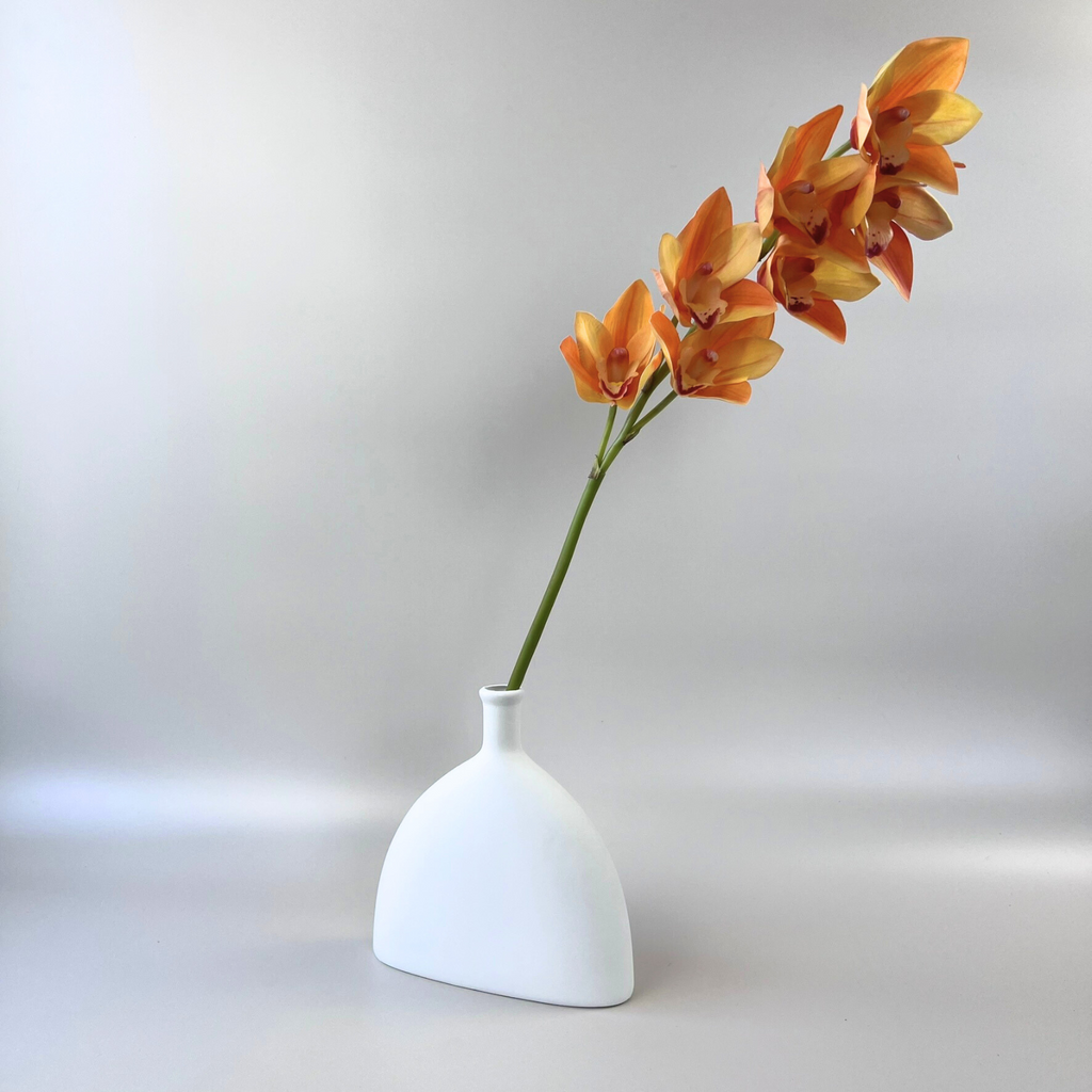 A single Real Touch Orchid Cymbidium floral stem with yellow and orange petals in a small white vase against a plain background