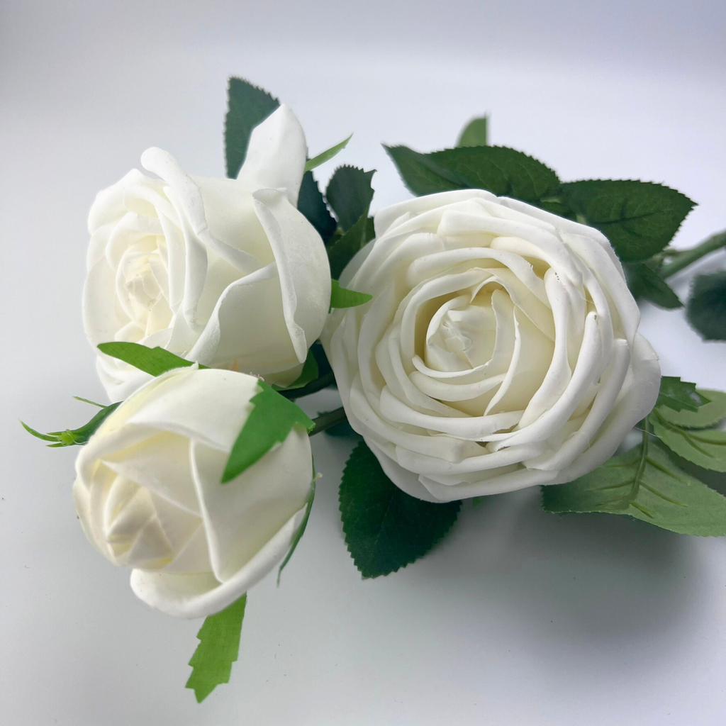 Close up of three white roses with realistic petals and green leaves against a plain background