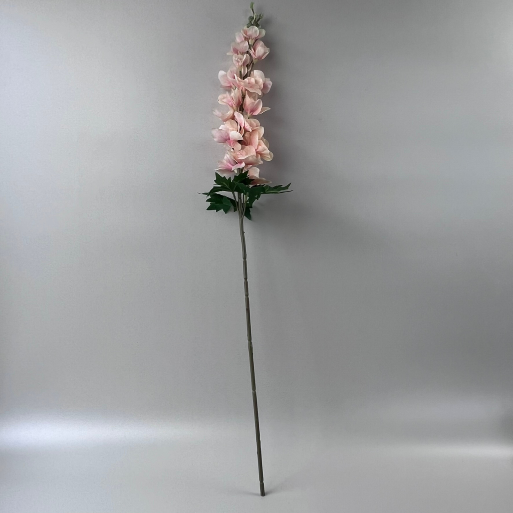 Single faux delphinium stem with pink flowers and green foliage against a plain background