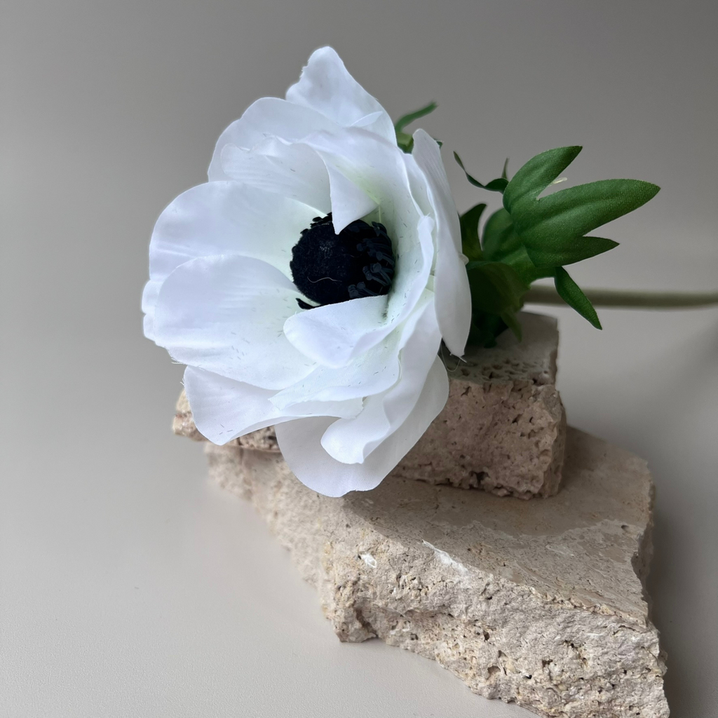 Artificial White Anemone with lifelike white petals and a striking dark centre lying on top of two small, natural pieces of stones