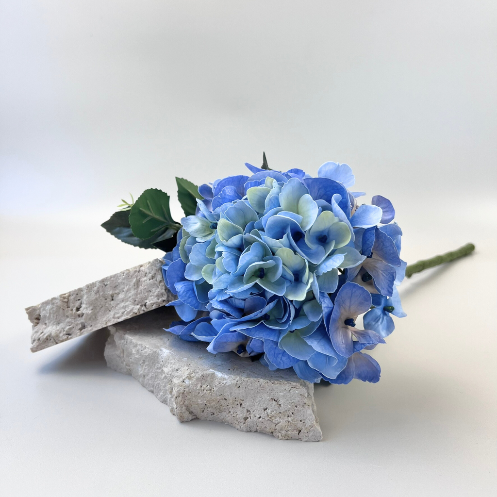 A faux Real Touch Hydrangea Macey with soft, green-blue petals styled on two decorative stones