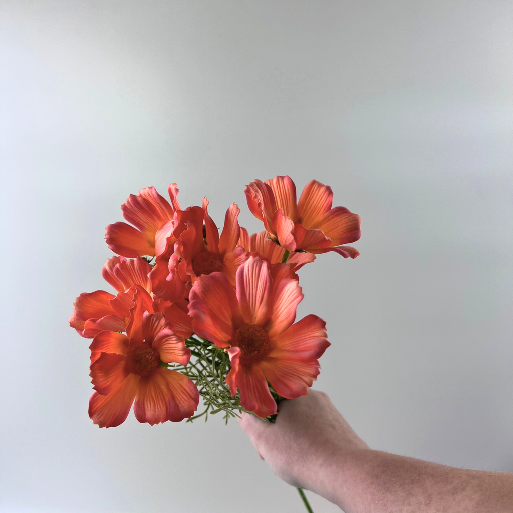Hand holding a bouquet of realistic Skimmia orange flowers against a plain background