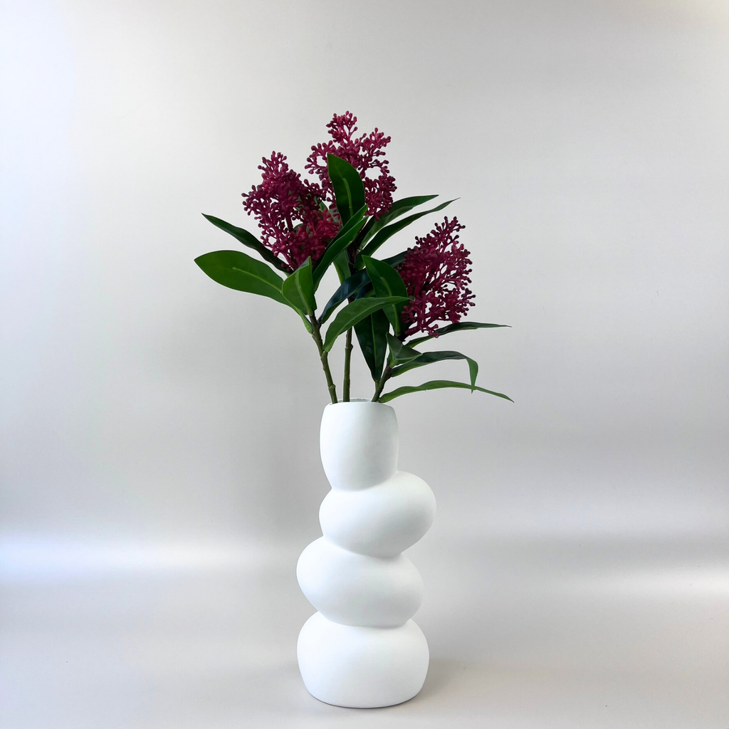 Three realistic Skimmia branches with deep red berries and green foliage in a structural white vase against a plain background