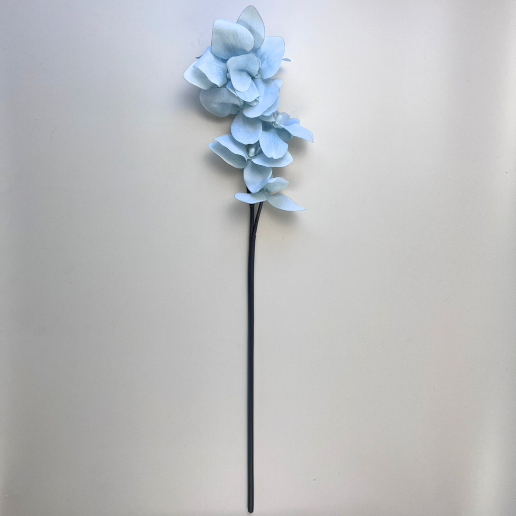 A faux Real Touch Phalaenopsis Orchid stem with baby blue blooms laying on a plain background
