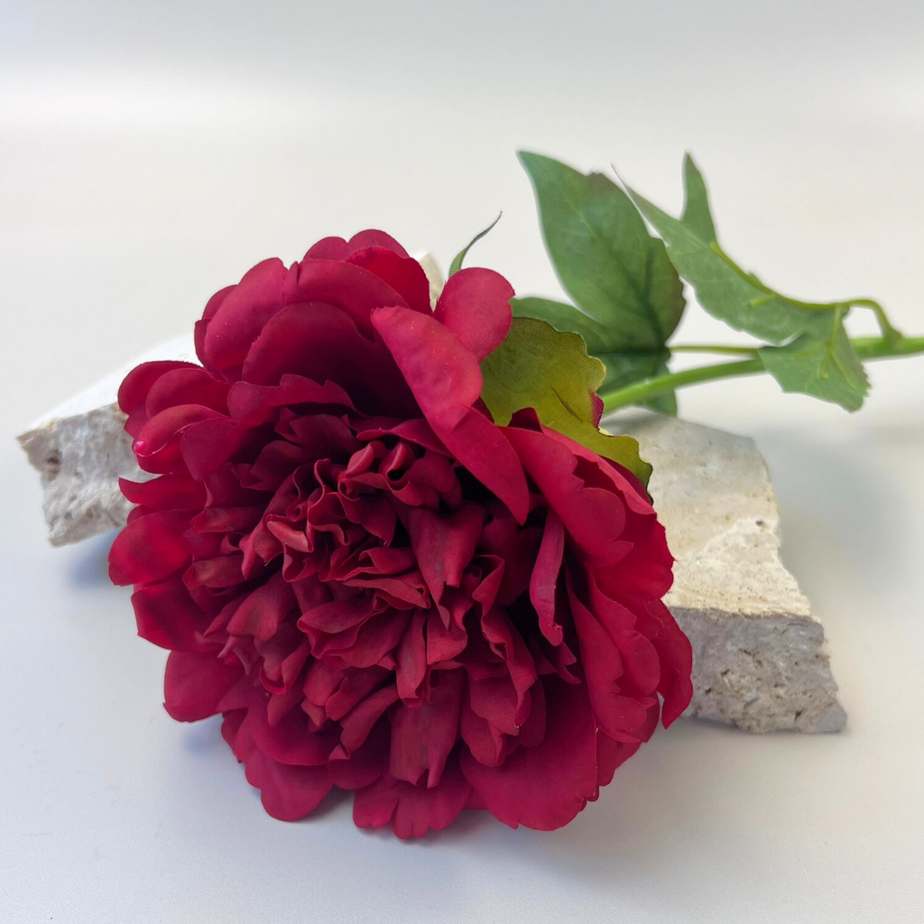 A red artificial peony flower styled on top of two small decorative stones against a plain background