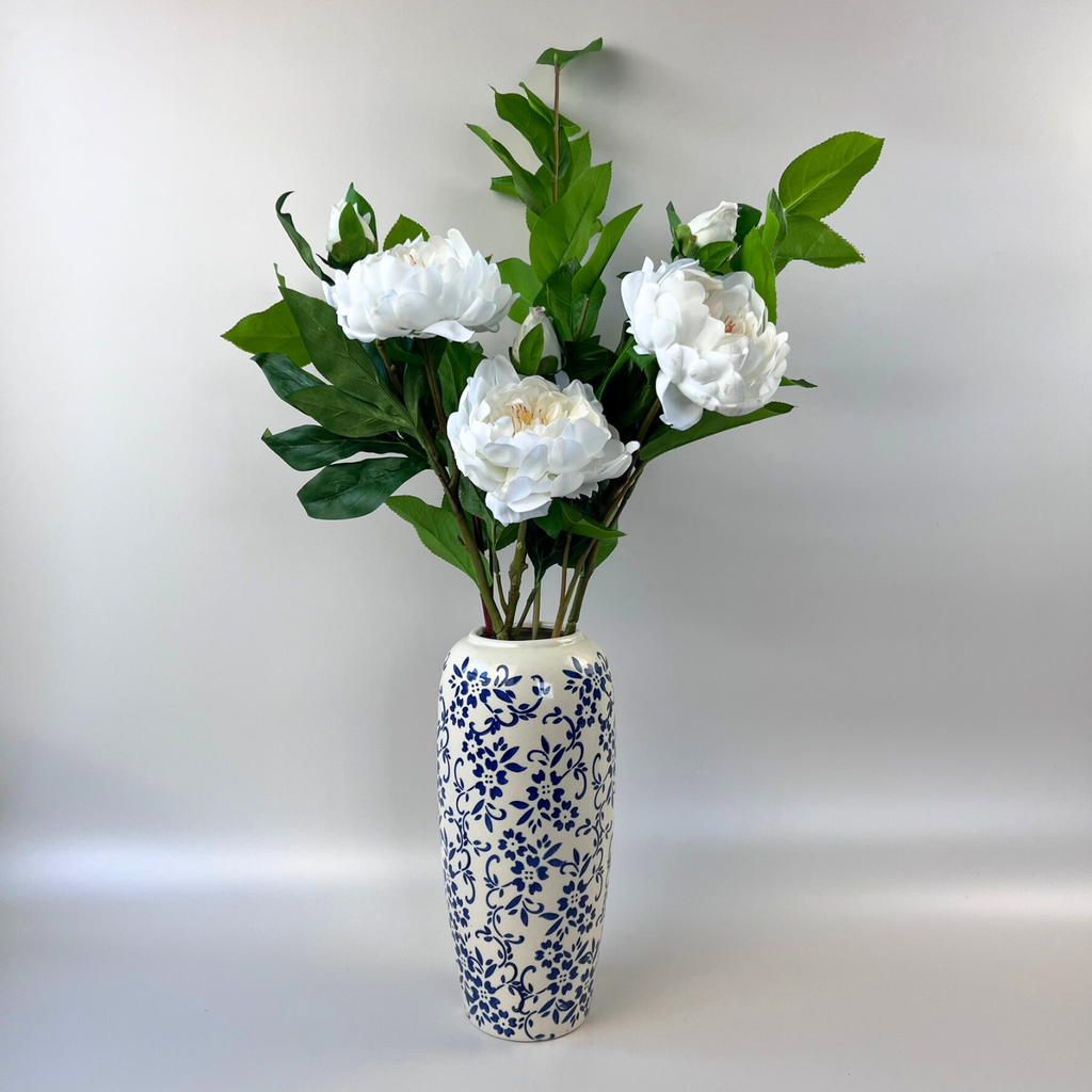 Ceramic vase styled with white flowers and green leaves on a plain background