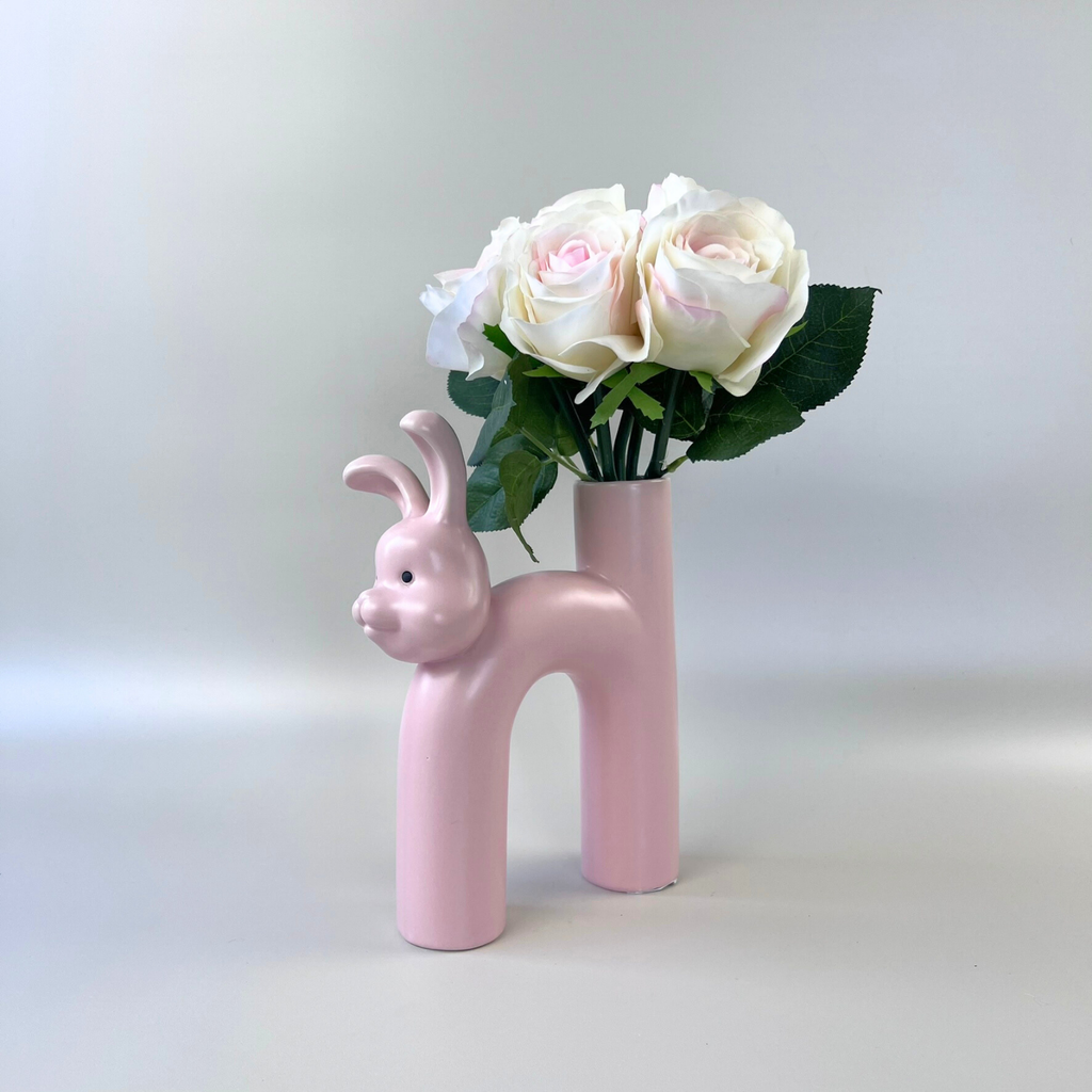 Pink rabbit shaped vase with a bouquet of flowers on a beige background