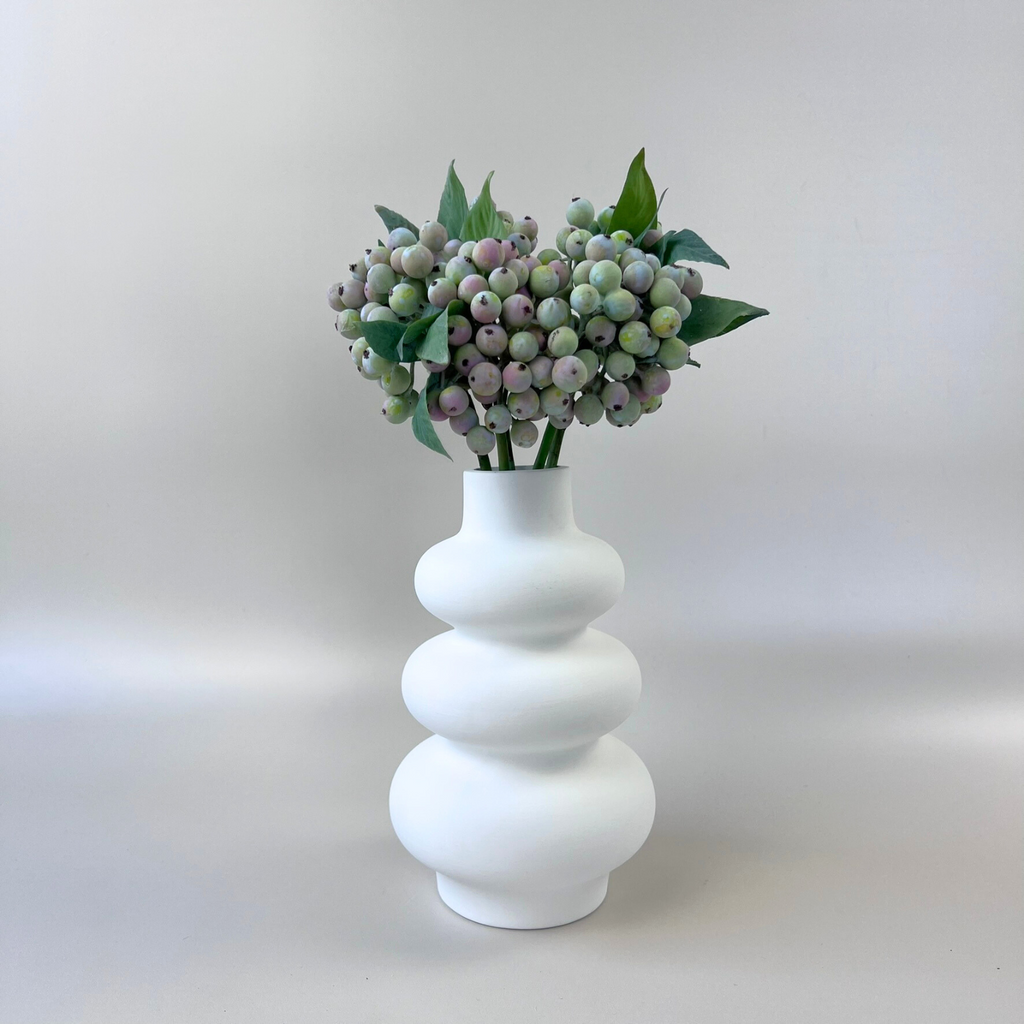 Green artificial berries in white curved vase